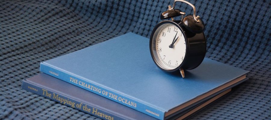 A black alarm clock sits on a stack of blue books.
