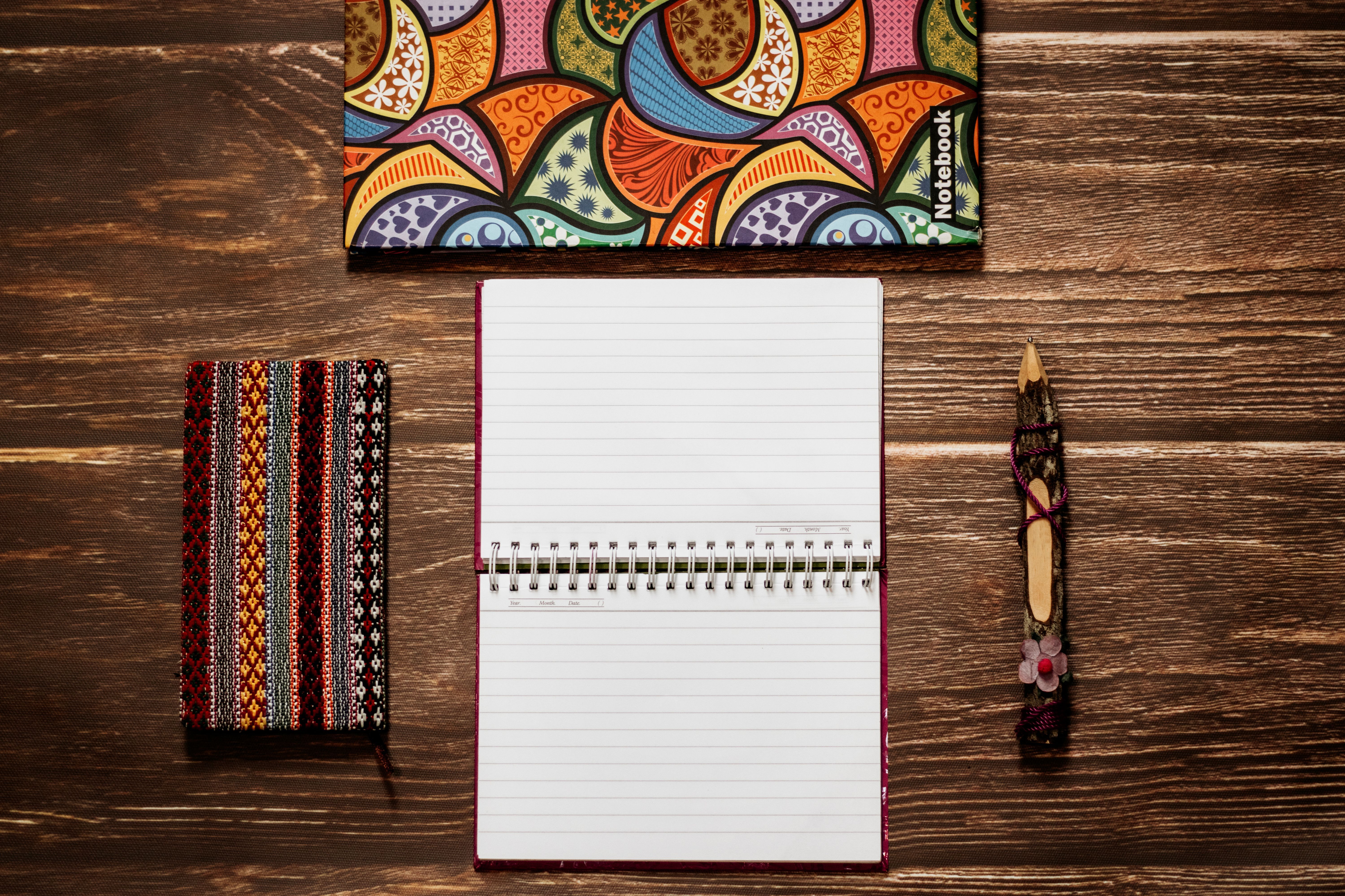 Colorful notebooks and a pencil arranged on a wooden table.