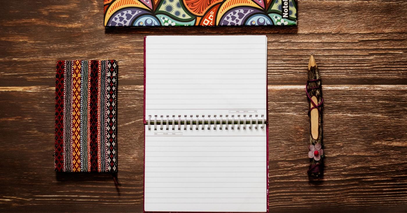Colorful notebooks and a pencil arranged on a wooden table.