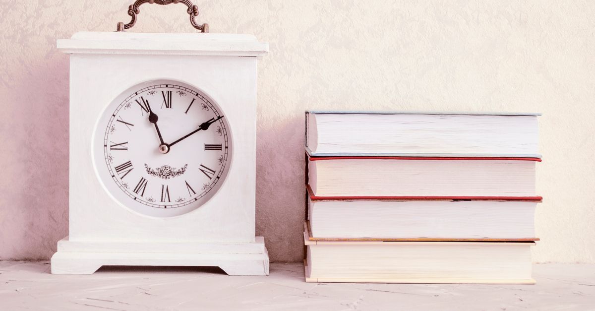 A white vintage clock beside a stack of books.