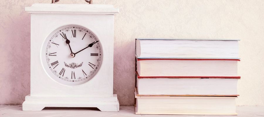 A white vintage clock beside a stack of books.