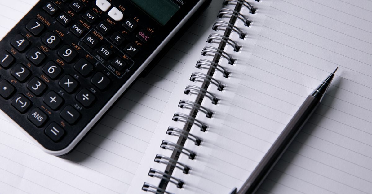 A calculator and pen beside an open notebook.