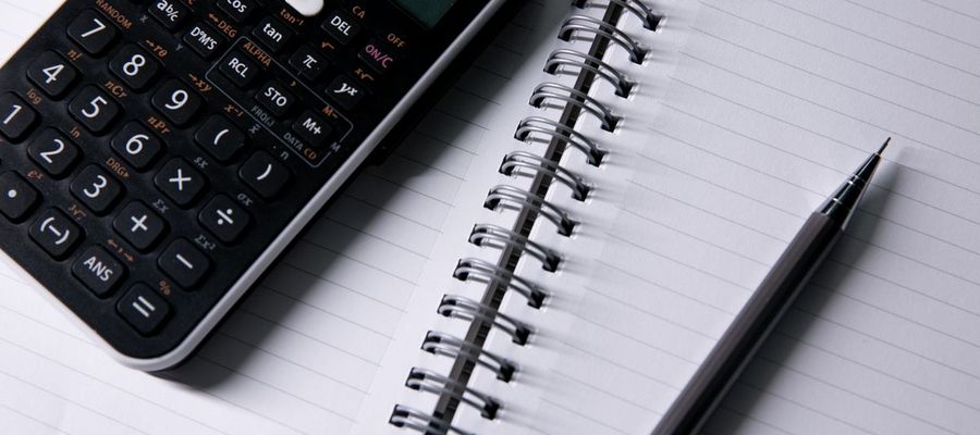 A calculator and pen beside an open notebook.