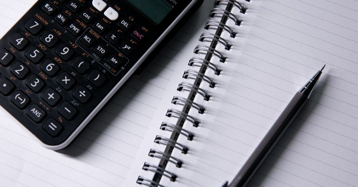 A calculator and pen beside an open notebook.
