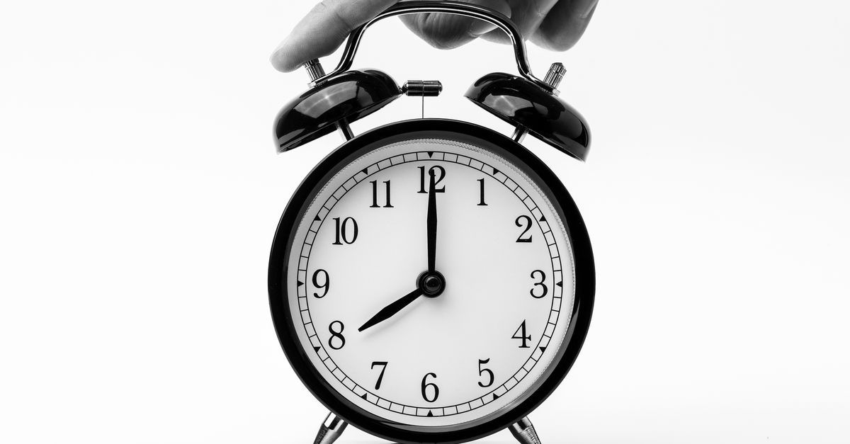 A hand reaches toward a black twin-bell alarm clock.