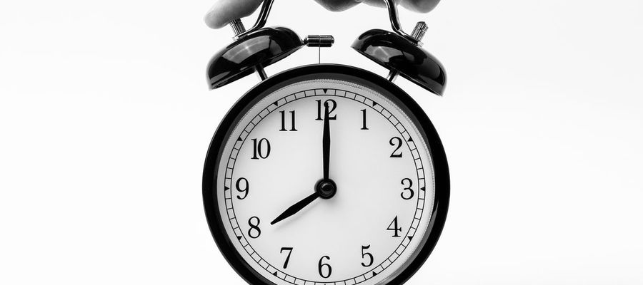 A hand reaches toward a black twin-bell alarm clock.