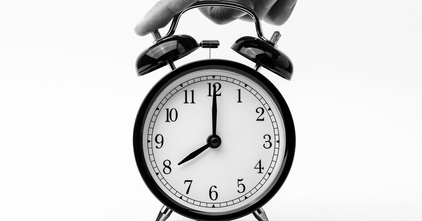 A hand reaches toward a black twin-bell alarm clock.