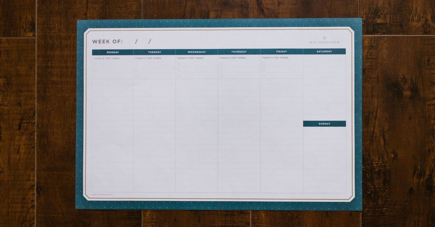 A blank weekly organizer lies on a wooden surface.