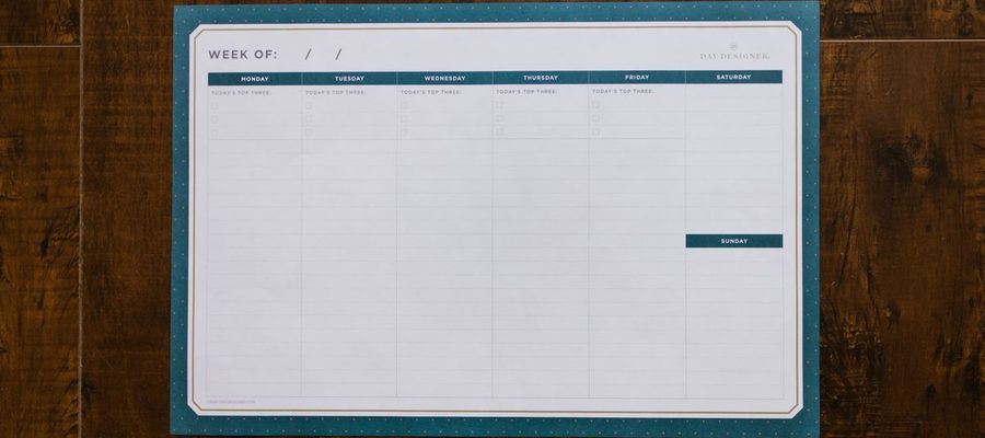 A blank weekly organizer lies on a wooden surface.
