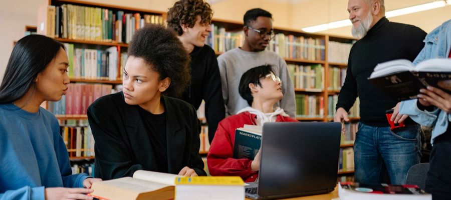 A group of students discuss study material at a university library table.