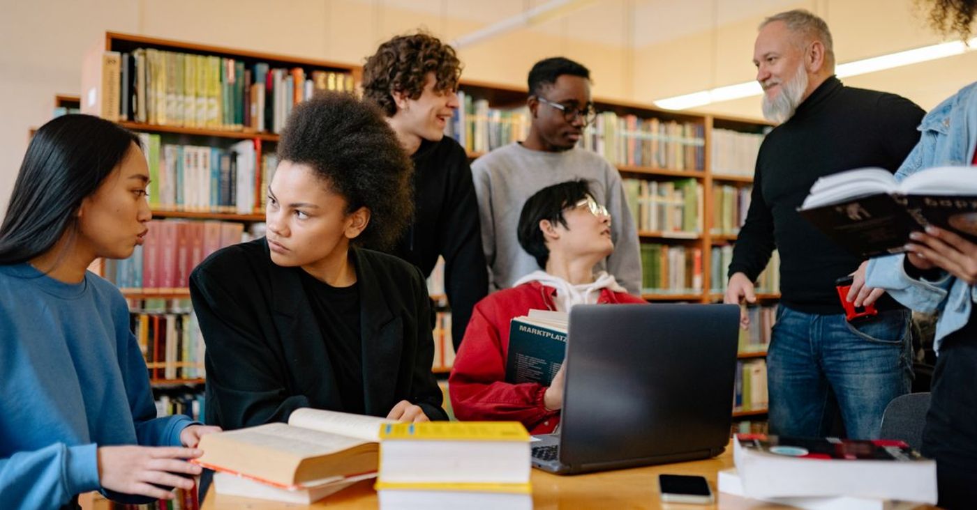 A group of students discuss study material at a university library table.