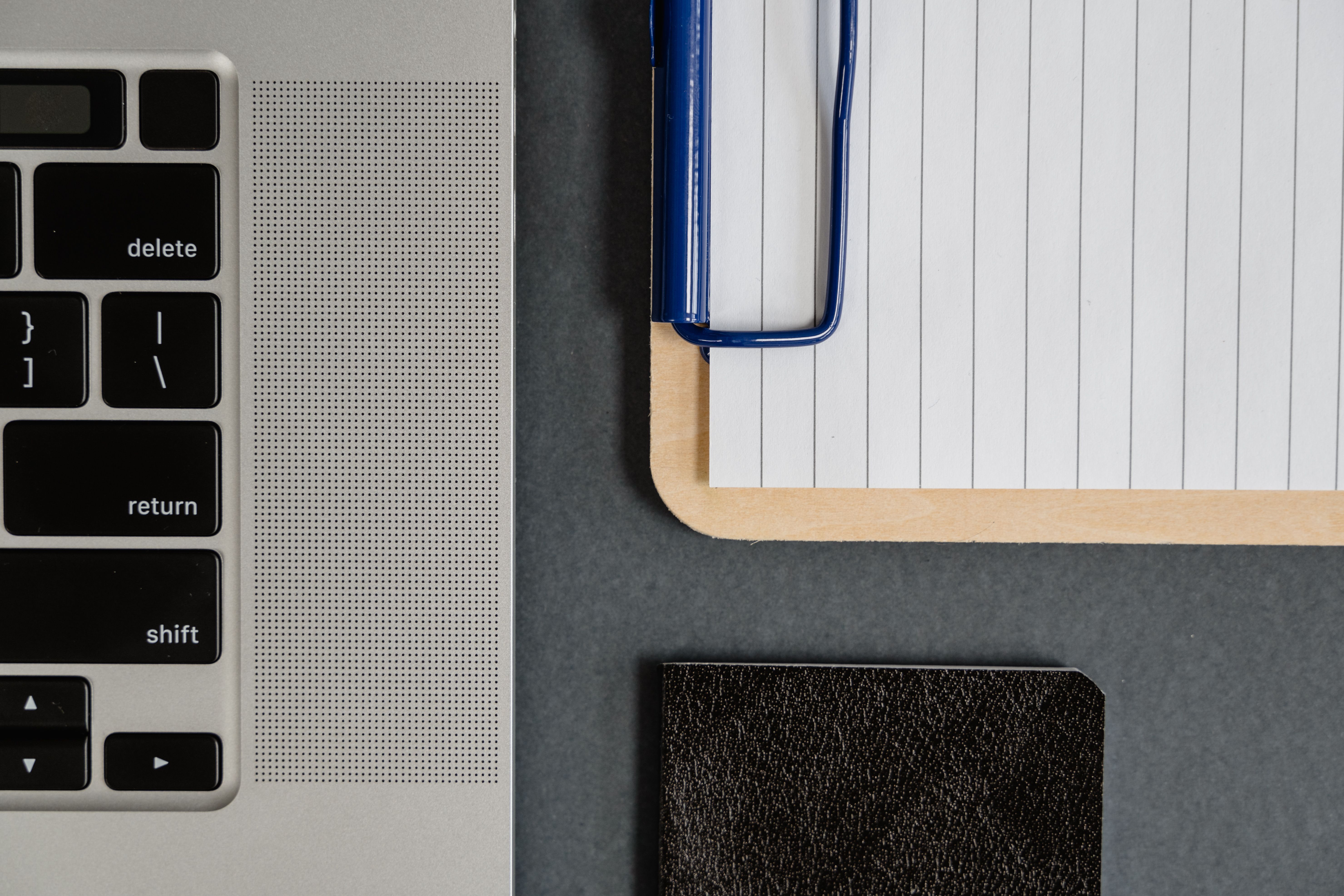 Close-up of a laptop keyboard beside lined paper on a clipboard.