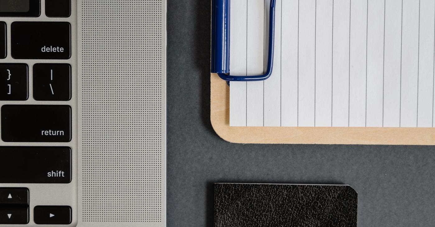Close-up of a laptop keyboard beside lined paper on a clipboard.