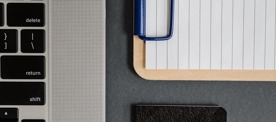Close-up of a laptop keyboard beside lined paper on a clipboard.