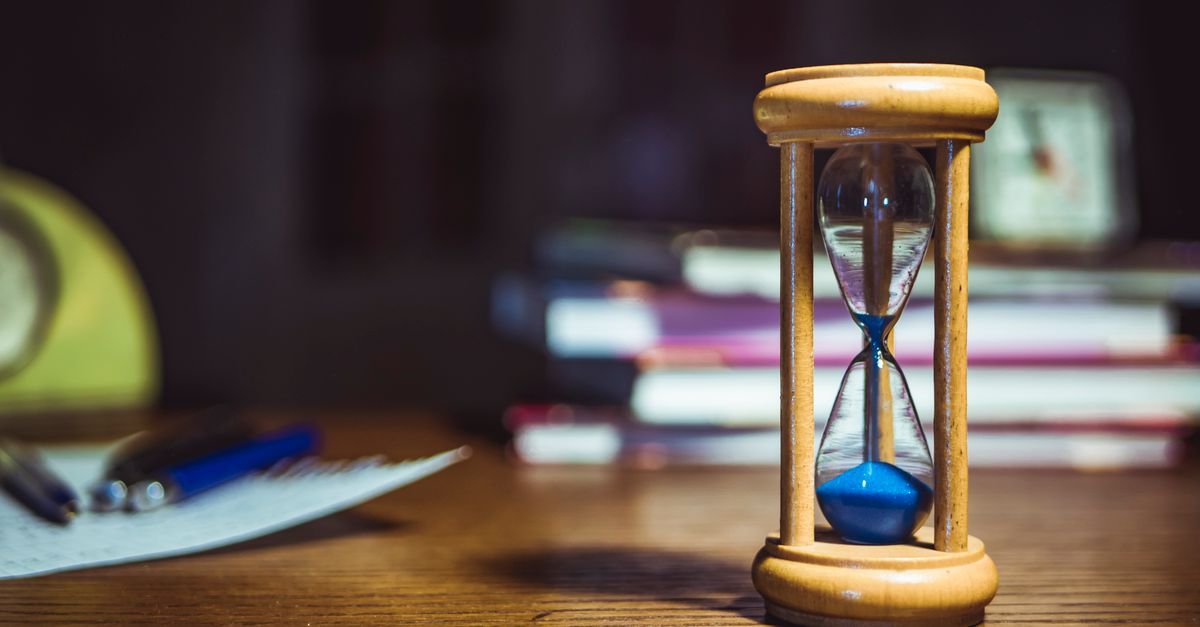 A wooden-framed hourglass beside books and pens on a desk.