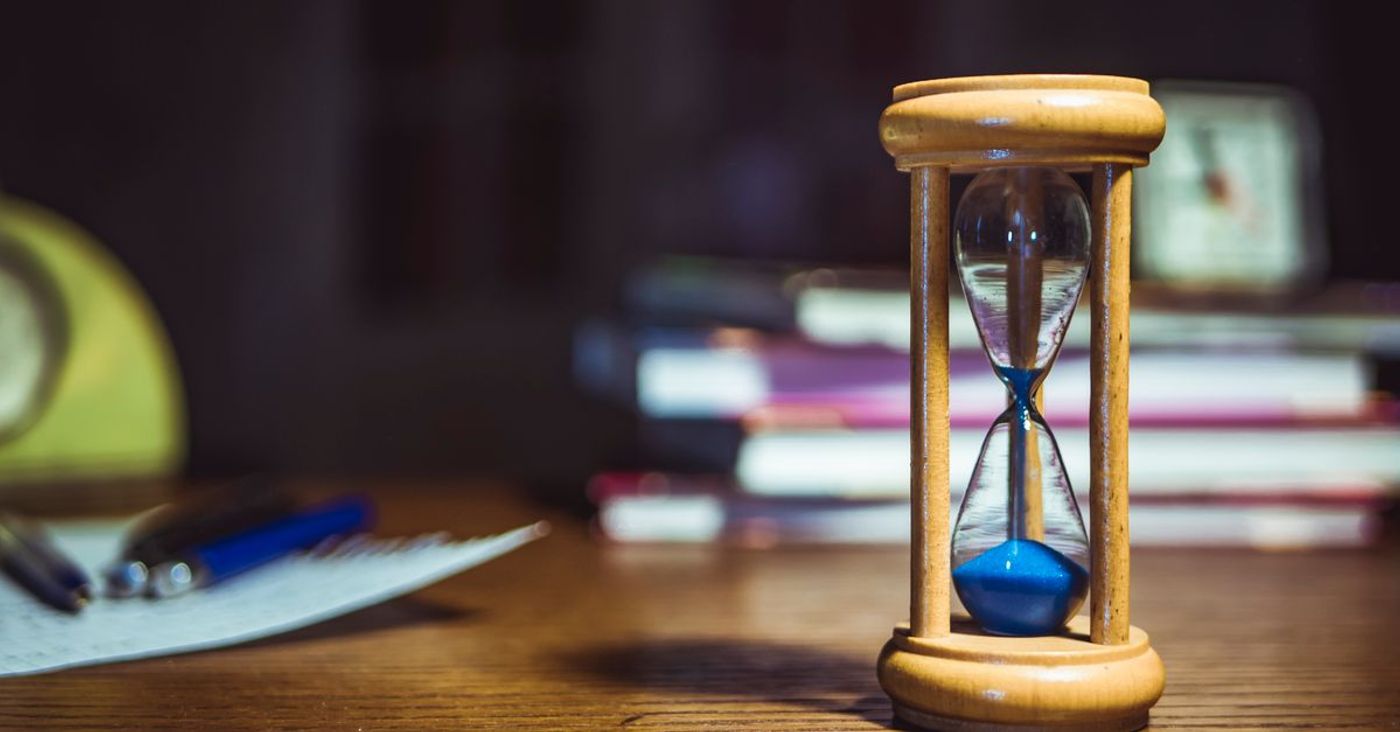 A wooden-framed hourglass beside books and pens on a desk.