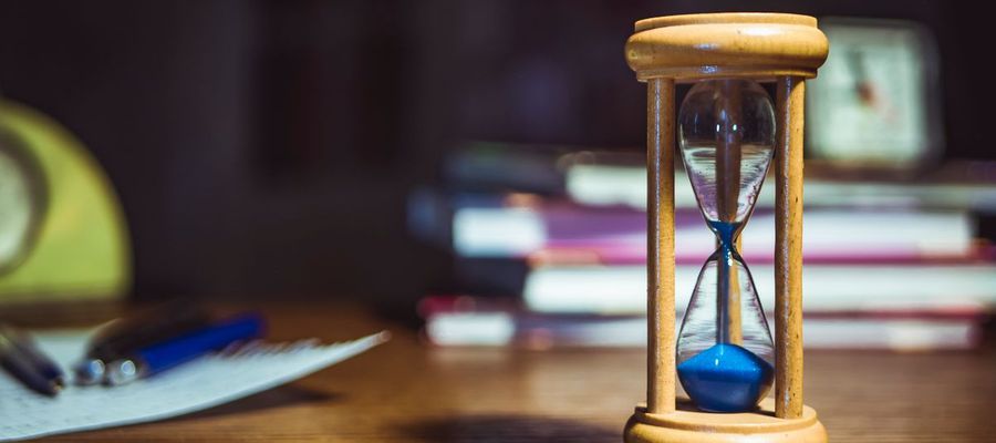 A wooden-framed hourglass beside books and pens on a desk.