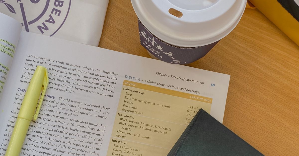 An open book, yellow highlighter, tablet and coffee on a wooden table.