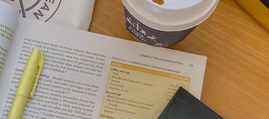 An open book, yellow highlighter, tablet and coffee on a wooden table.