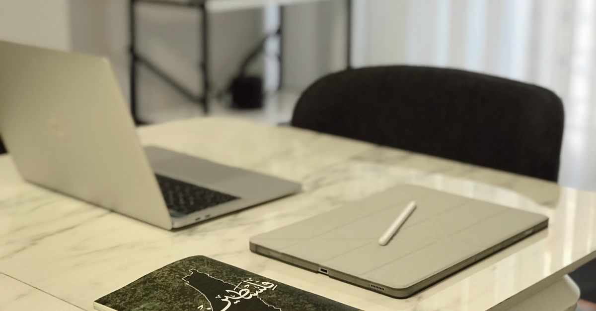 A laptop, tablet and book arranged on a marble table.