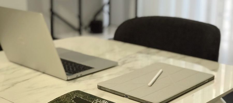 A laptop, tablet and book arranged on a marble table.