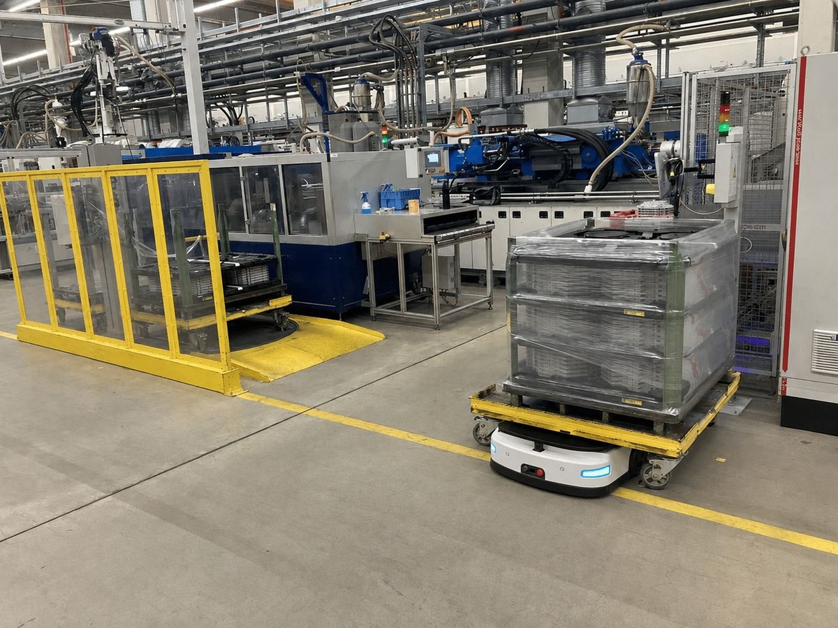 AGV transporting material racks beside injection molding machines and safety fencing