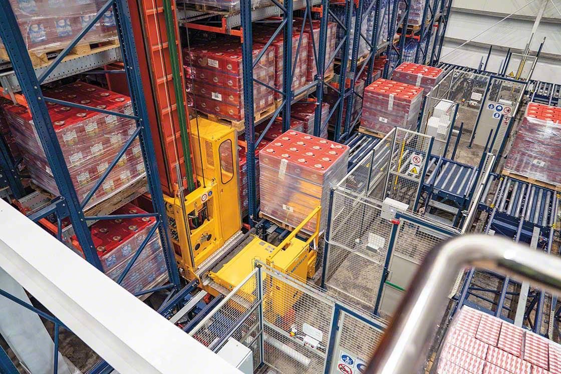 Automated stacker crane handling pallet loads beside conveyor equipment in an ASRS warehouse
