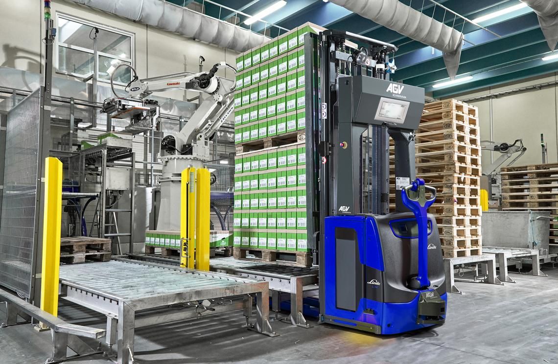 Automated forklift AGV moving pallet loads beside a conveyor and robotic arm