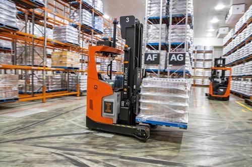 Driverless industrial truck transporting a wrapped pallet through warehouse aisles