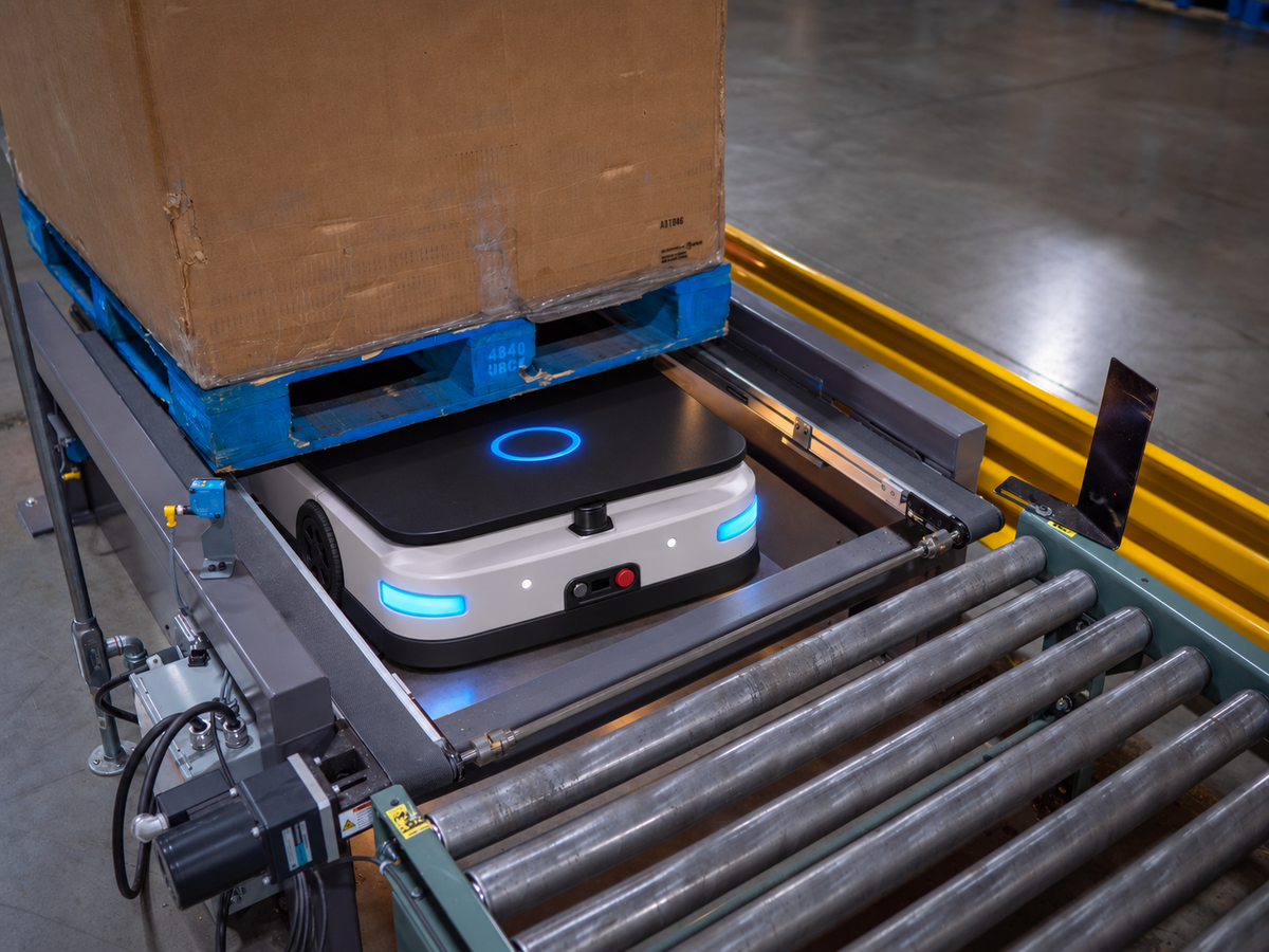 Conveyor AGV docked at a roller transfer station beneath a palletized load