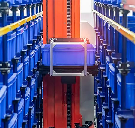 Automated tote storage and retrieval equipment handling a blue bin between storage racks