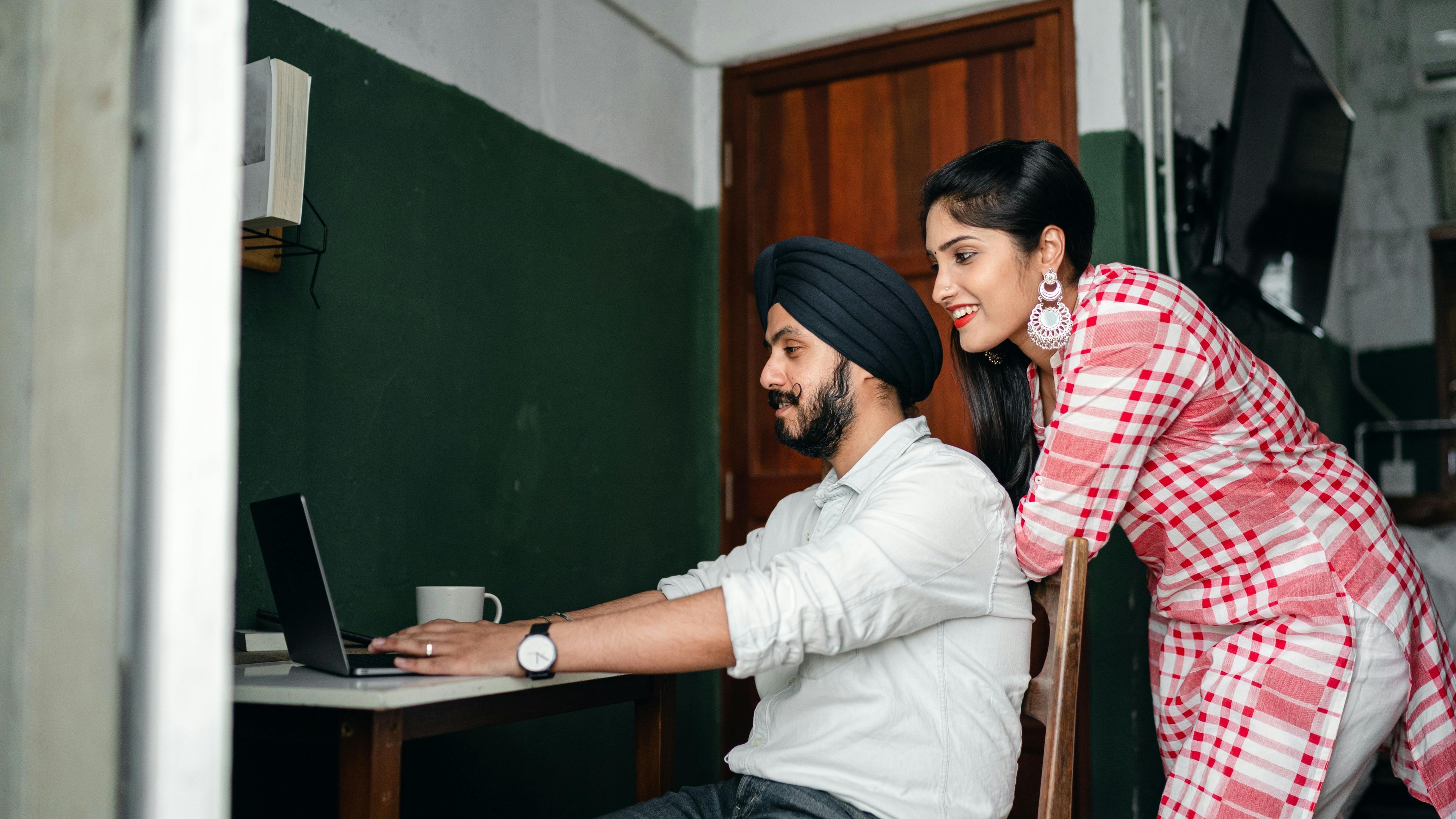 a woman is standing next to a man using a laptop computer .