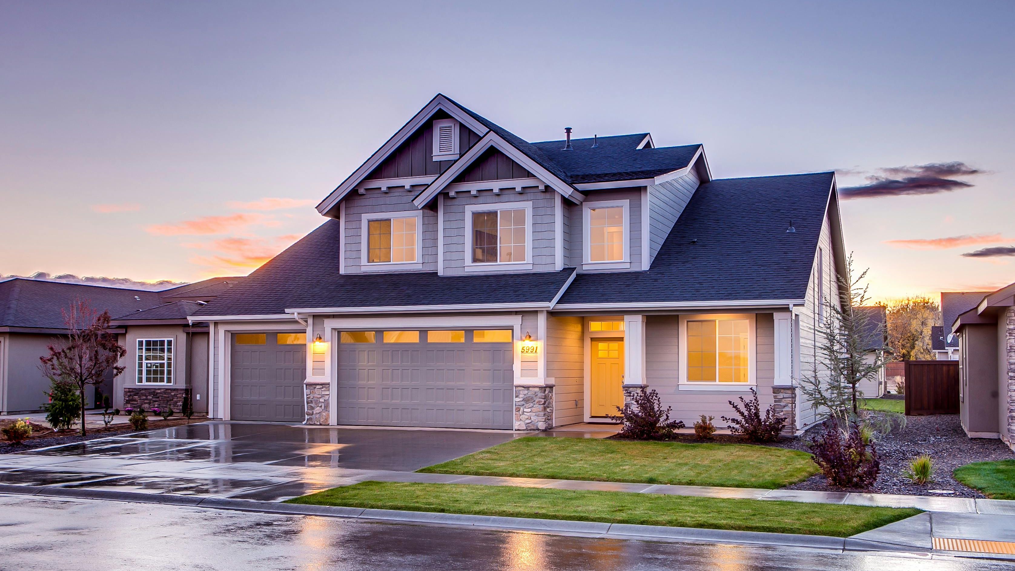 a large house with two garages and a lush green lawn is lit up at sunset .