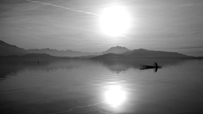Sol refletido num lago entre montanhas, em preto e branco