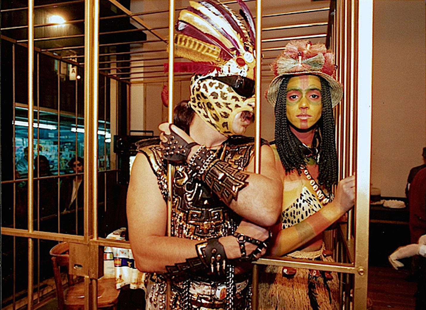 Guillermo Gómez-Peña & Coco Fusco inside a golden cage dressed in native costume.