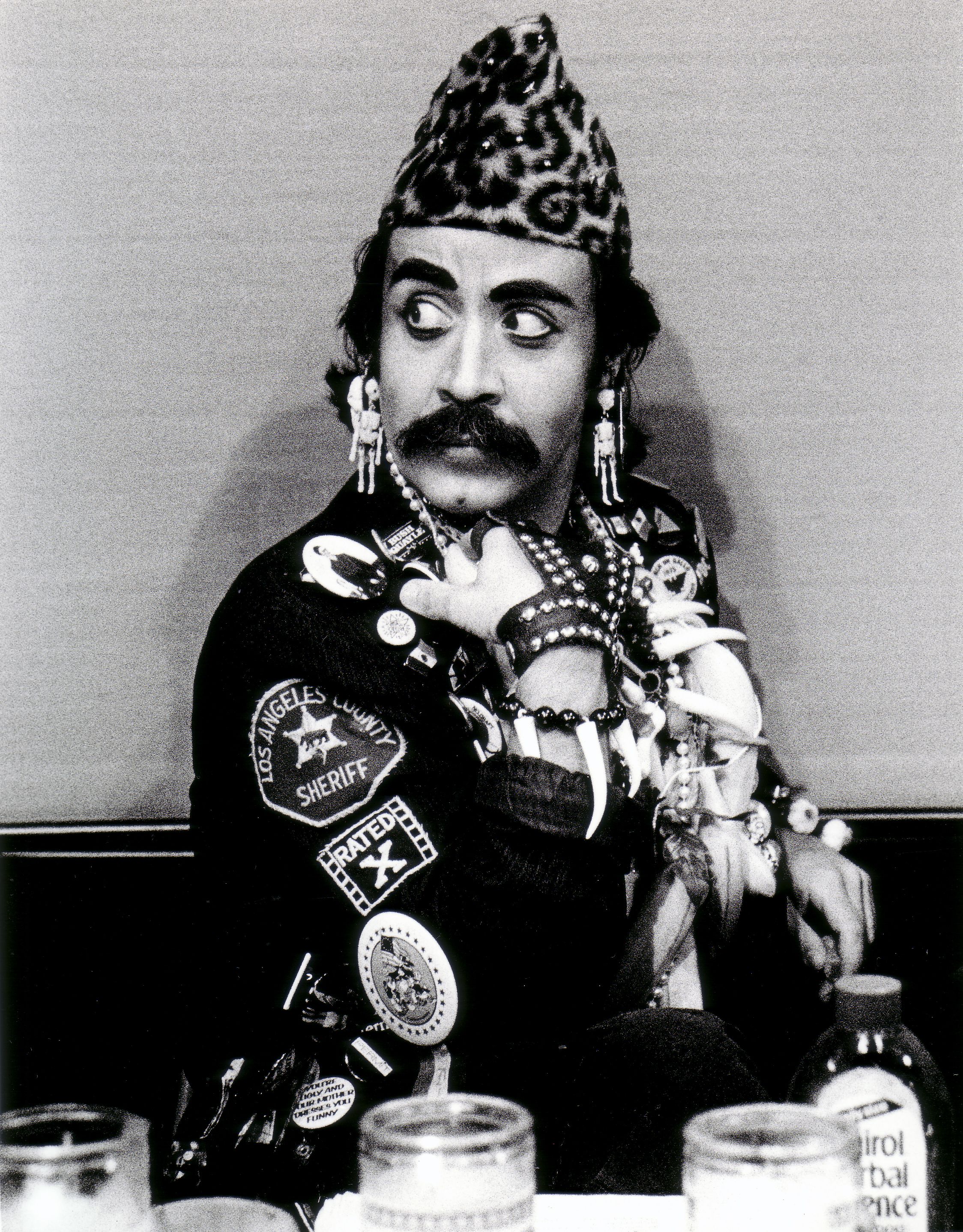 Guillermo Gómez-Peña in a leopard fur cap seated behind candles and ritual ephemera.