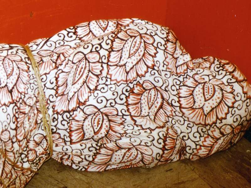 Guillermo Gómez-Peña positioned on the floor in a public elevator. Wrapped in floral-patterned batik fabric.