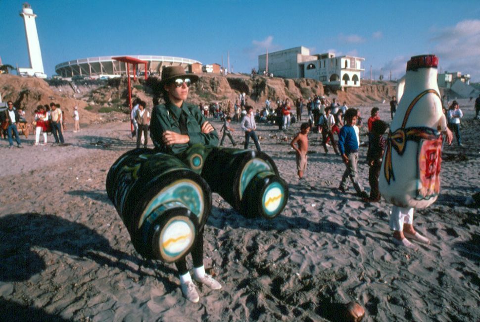Border Arts Workshop performers dressed up as binoculars and a bottle on a beach.