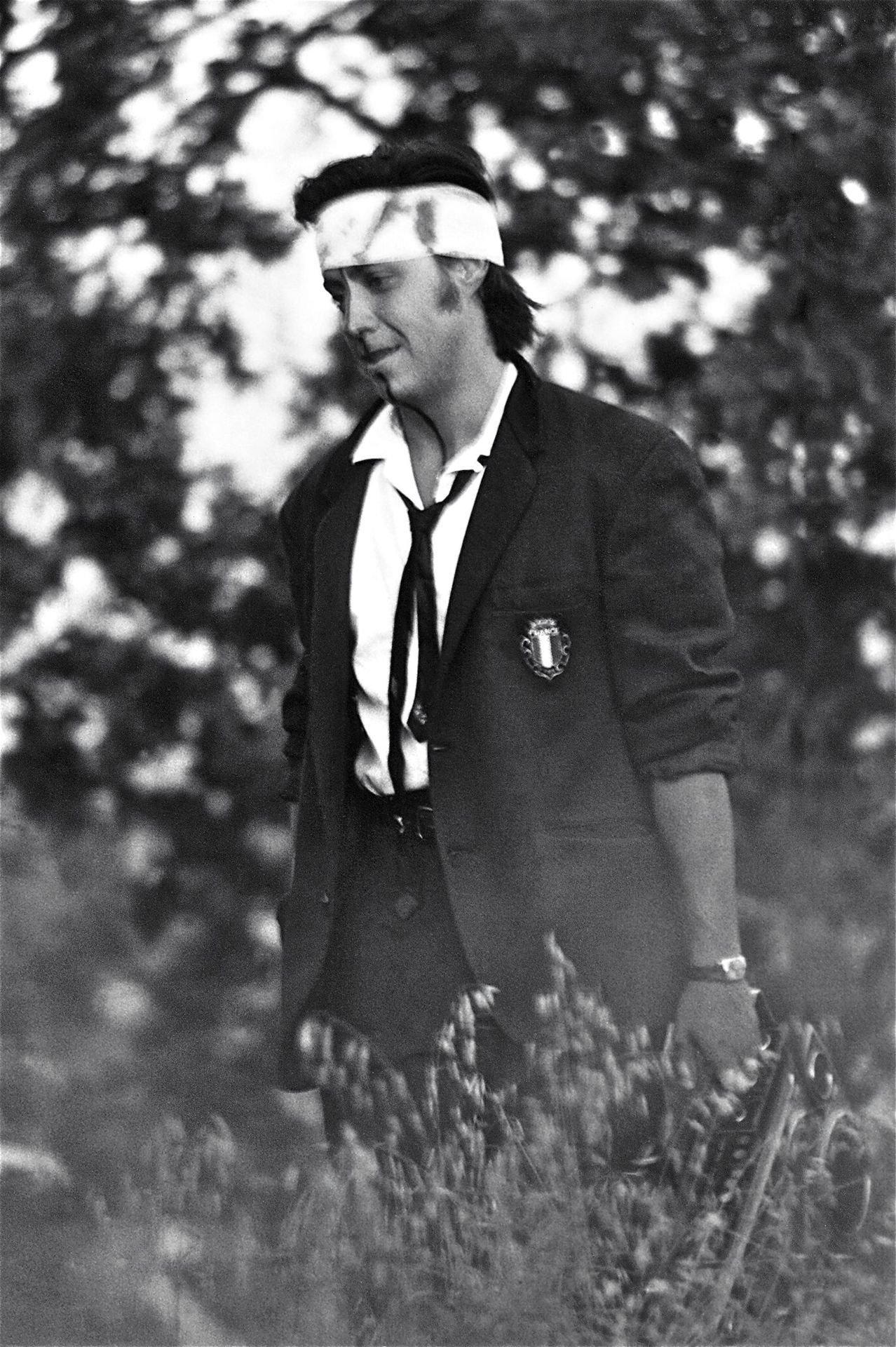 Guillermo Gómez-Peña walking across the desert in a suit with a bandage on his head.