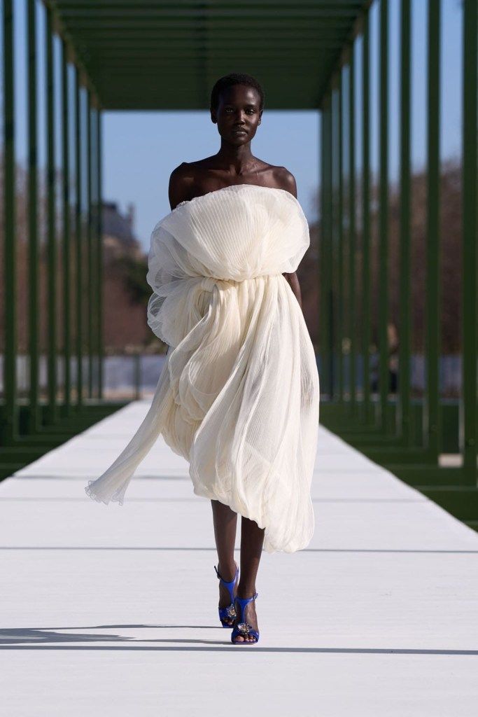 A runway wide shot from Fall/winter 2026-27. Structured tailoring, clean architectural silhouettes. Controlled palette. Muted editorial color grading.