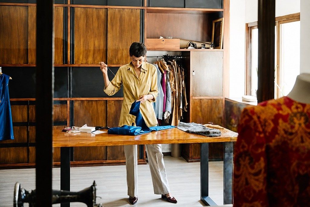 wide editorial shot of an atelier or small production space. A tailor working by hand in a natural light. The image communicates that something real is being made.