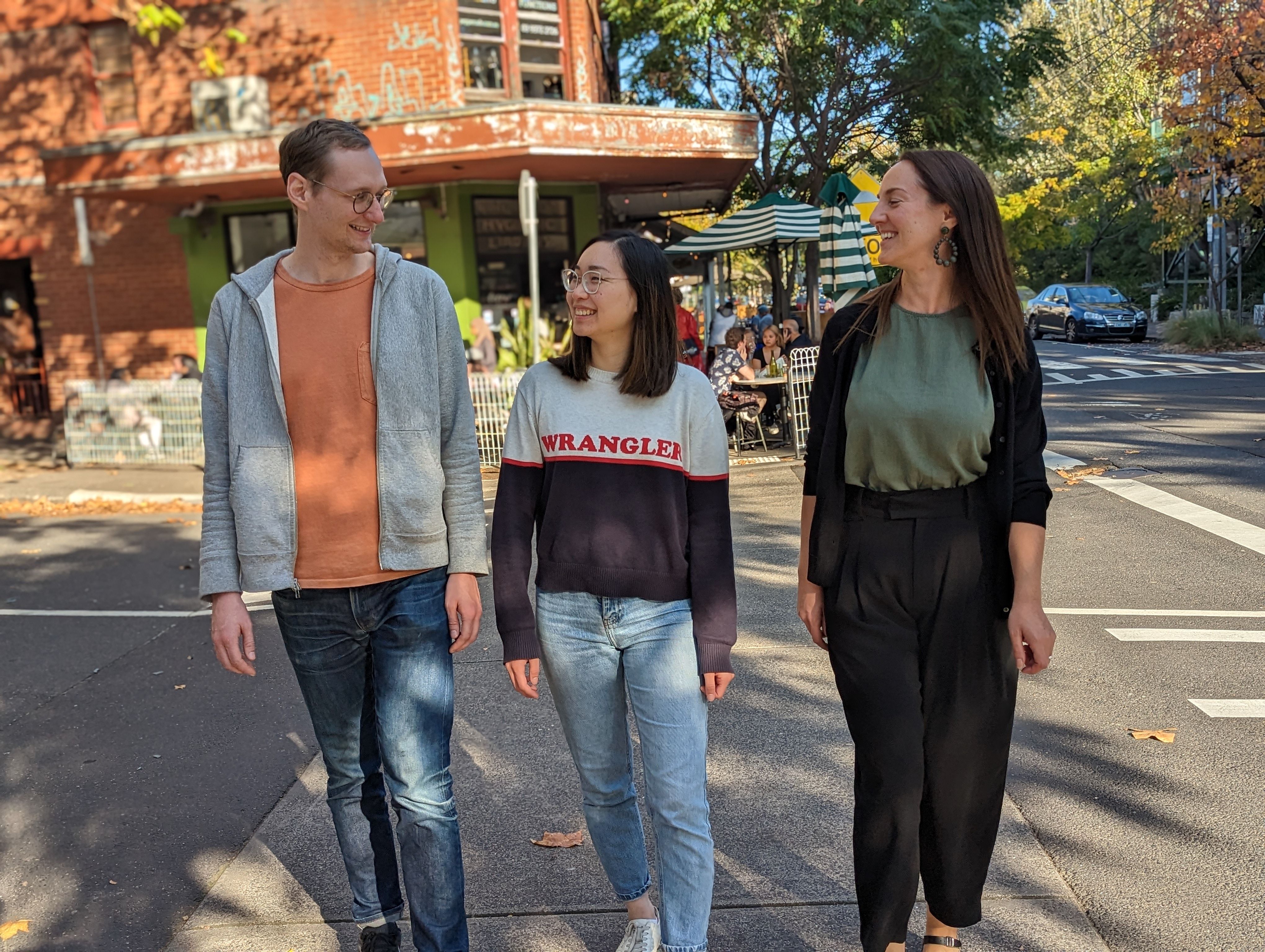 Three people standing next to a street intersection smiling and laughing.