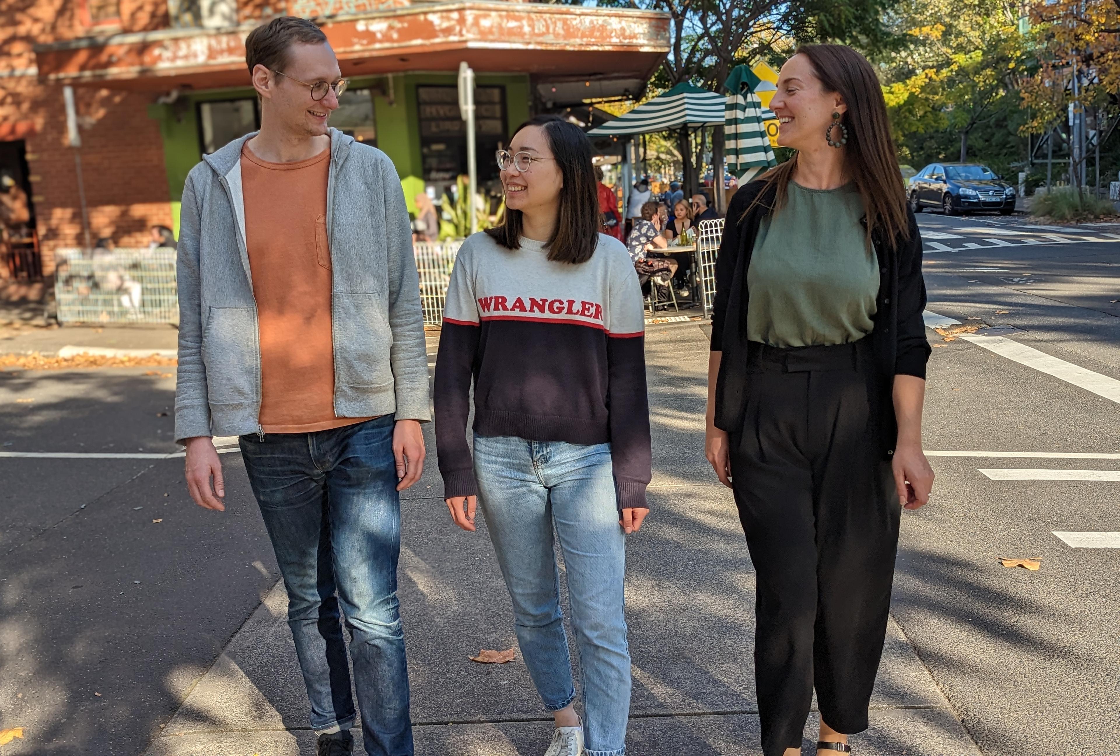Three people standing next to a street intersection smiling and laughing.