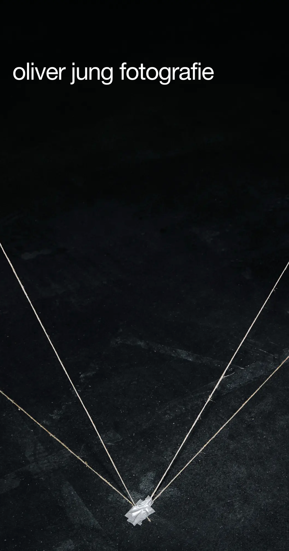 Screenshot from the mobile website showing oliver jung fotografie and a picture of strings taped to a black floor