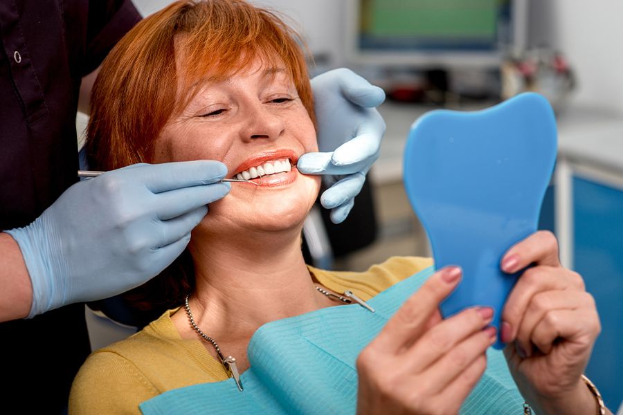 Middle-aged woman smiles at the mirror in a dentist’s chair, happy she has the best restorative dentist in San Francisco