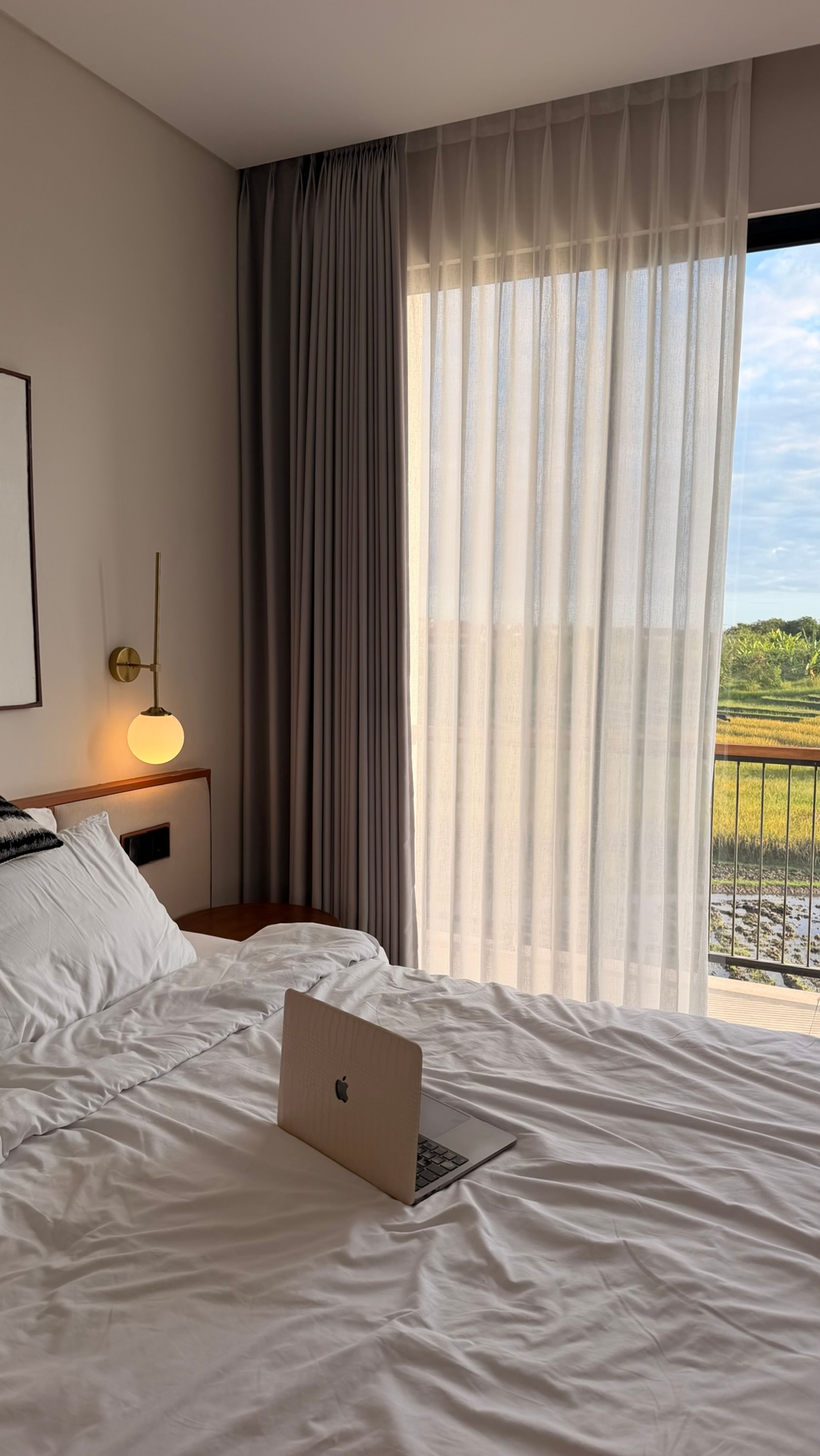 Laptop on a bright bed in front of a large window