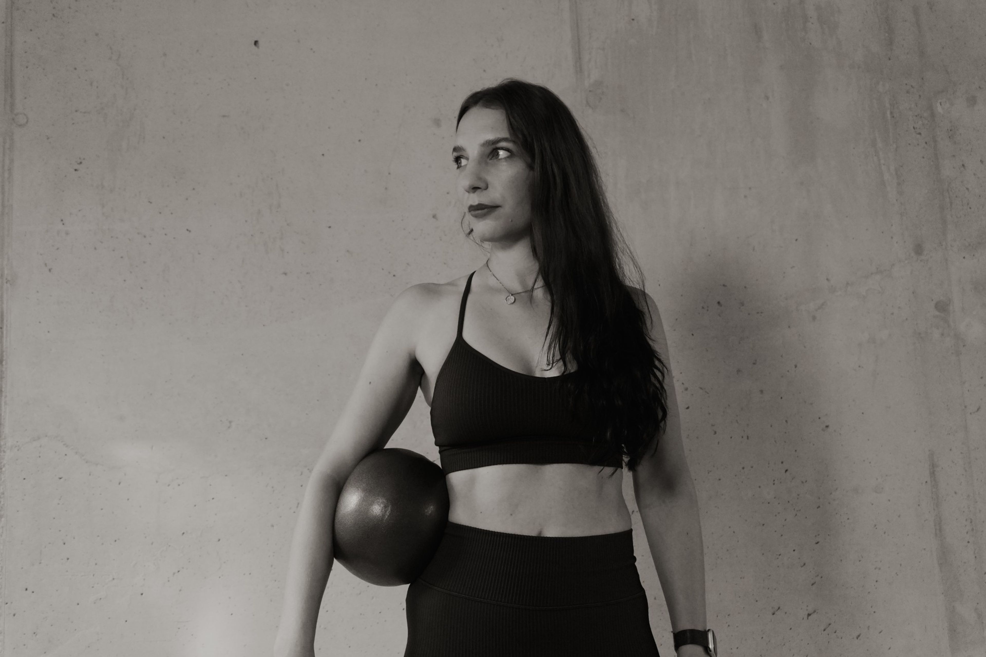 Corinna from Salt8 holding a Pilates ball in front of a concrete wall