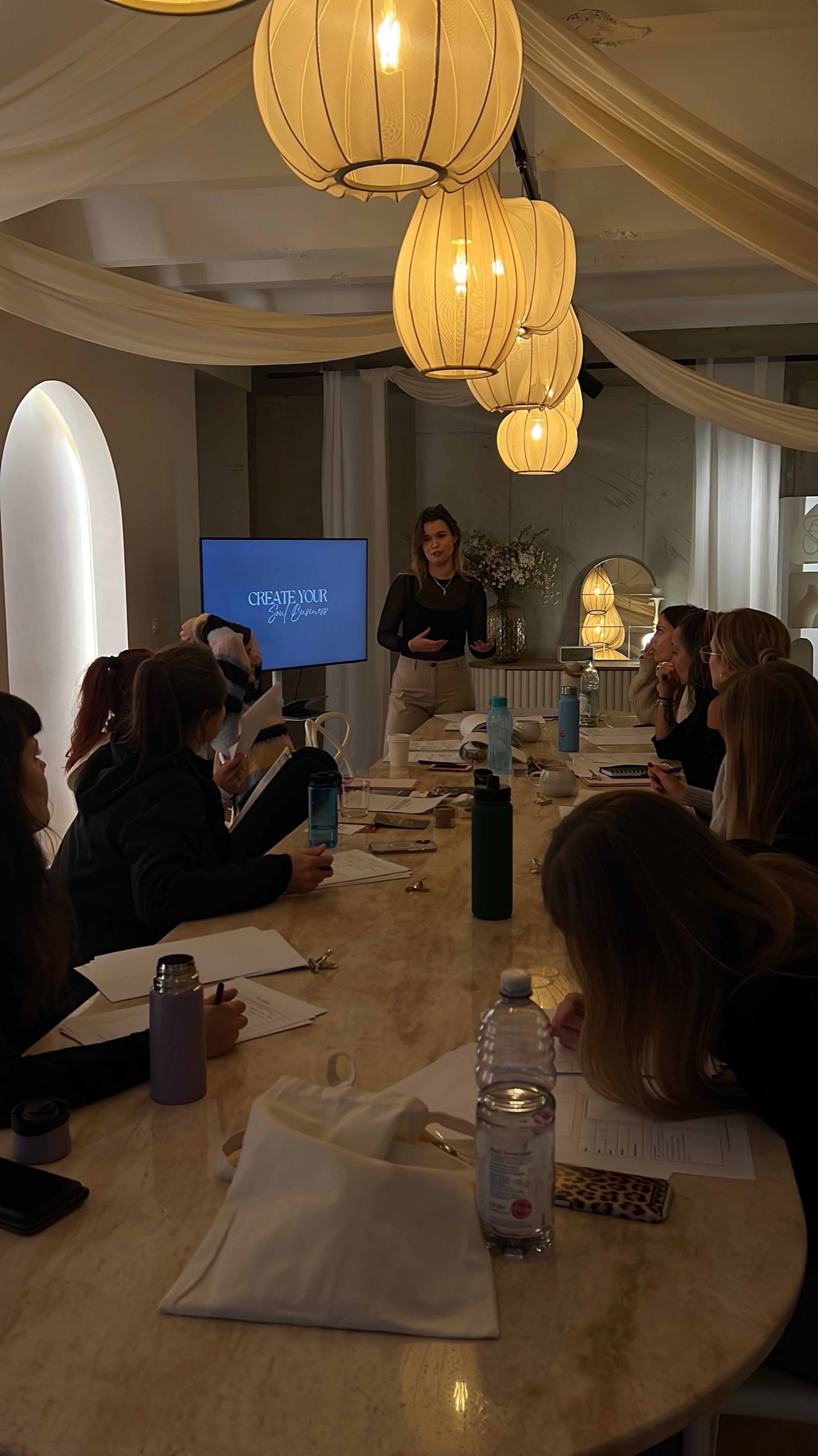 Saskia hält einen Workshop an einem langen Tisch unter warmen Lampen