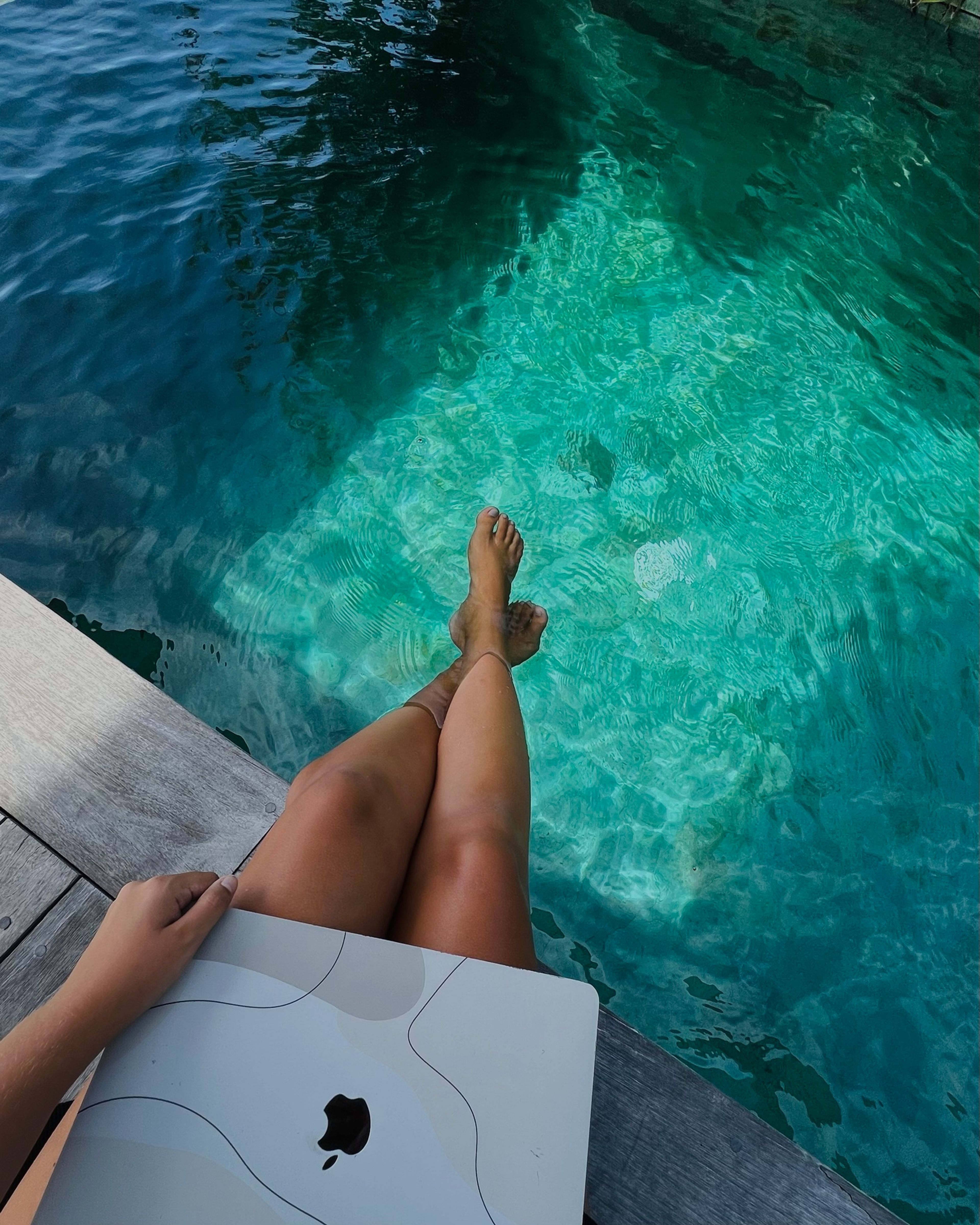 Legs in a turquoise pool next to a laptop