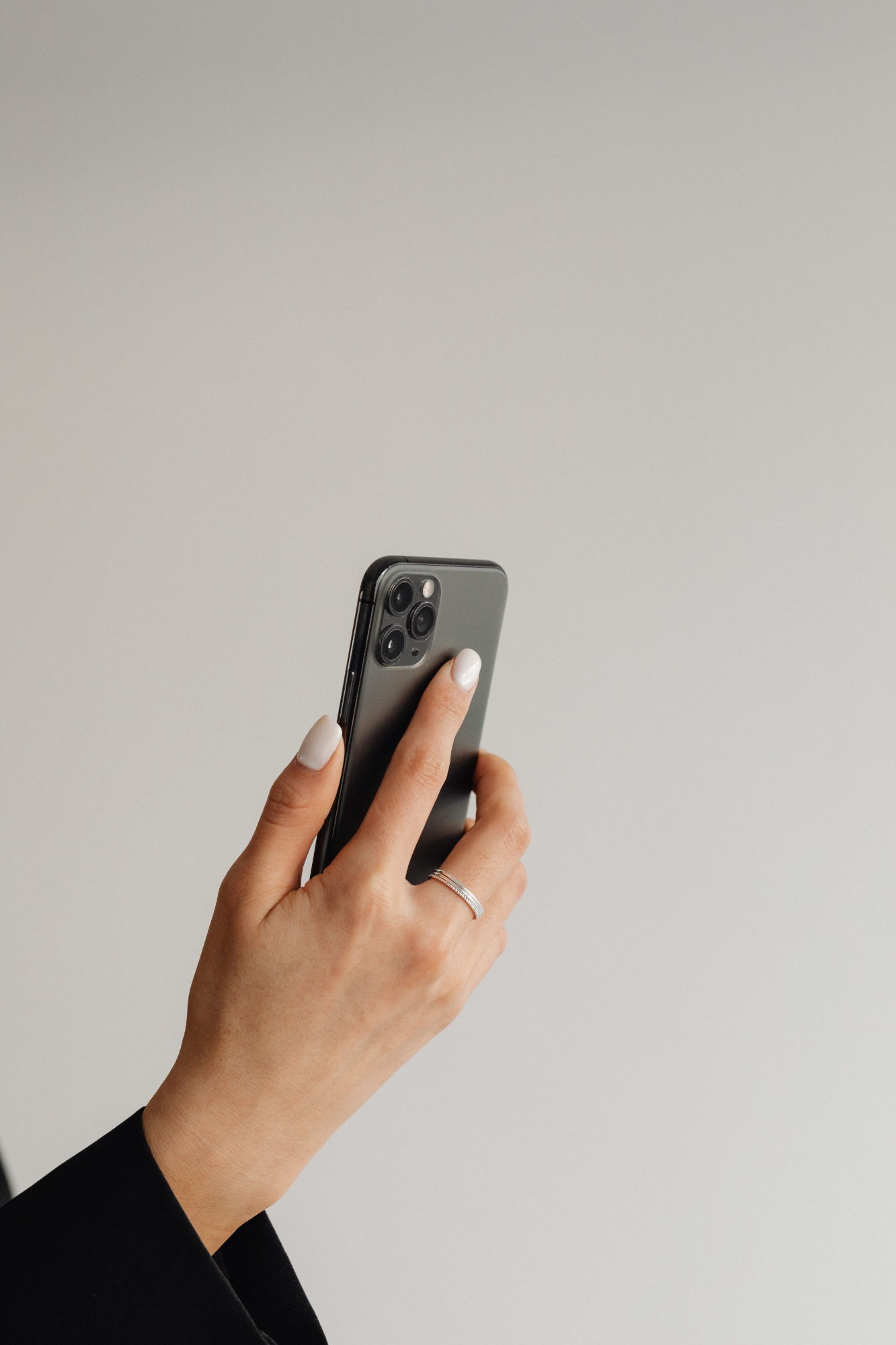Hand mit hellen Nägeln hält ein Smartphone vor heller Wand